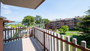 A balcony with a wooden railing overlooking a residential area with apartment buildings and greenery. - Appartamento Luisa e Francesco (Peschiera del Garda)