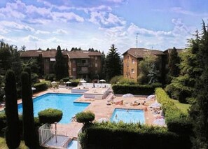 A hotel courtyard with multiple swimming pools, surrounded by well-maintained hedges and trees.