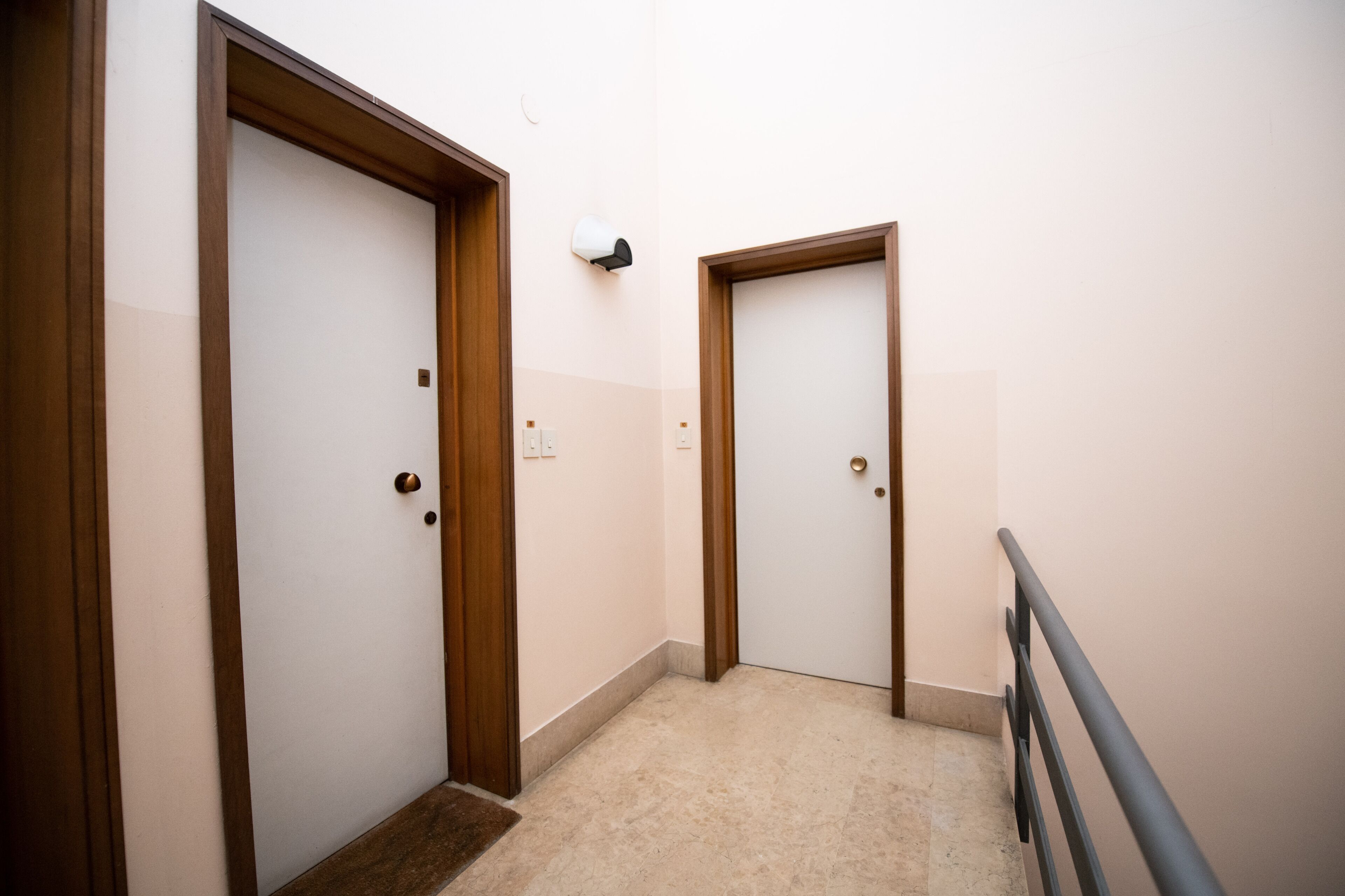 A hallway with two doors, a light switch, and a handrail.