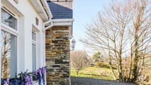 Een huis met een gevel van natuursteen, een grindpad en een bloembak met bloemen.