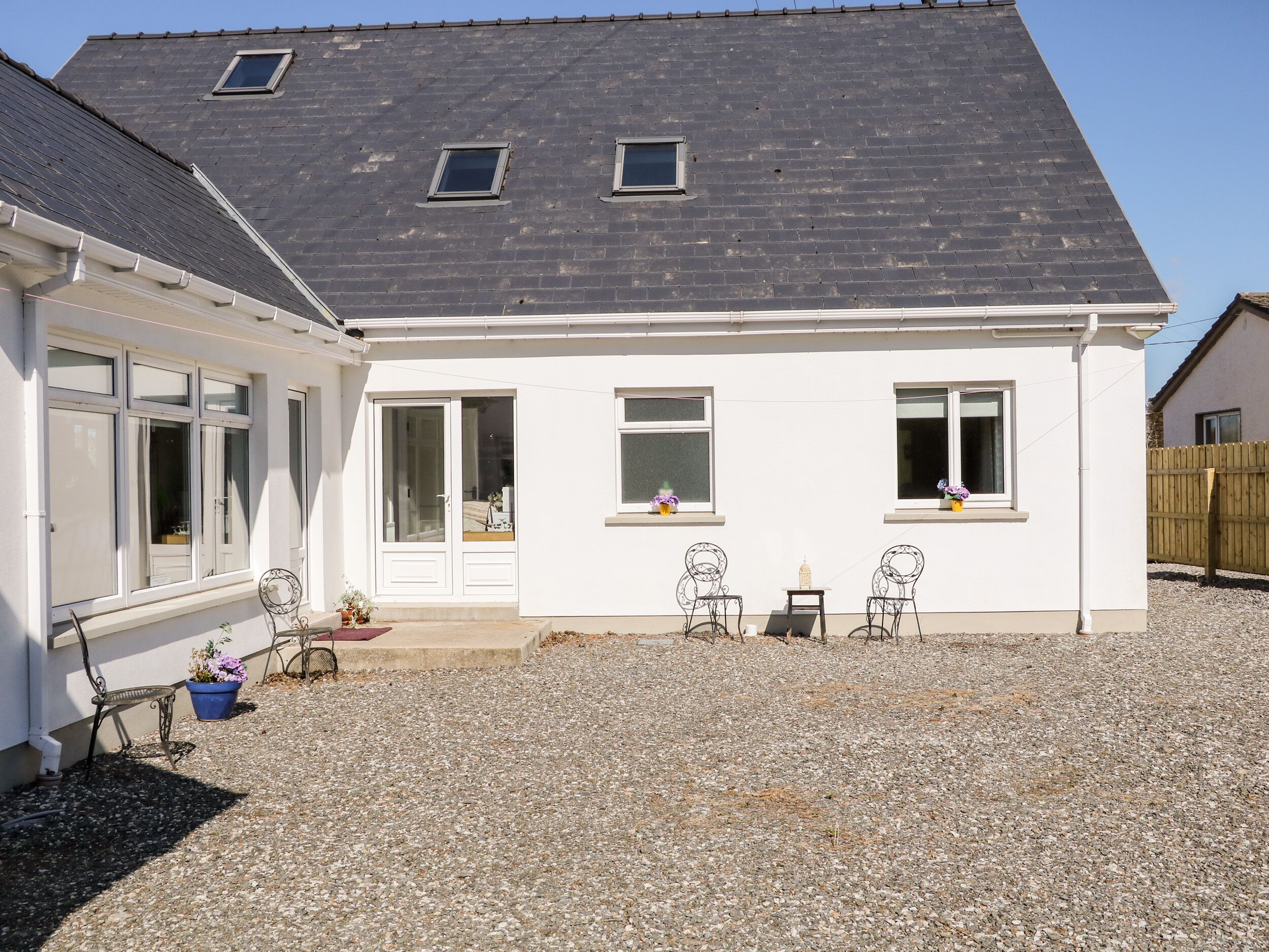 A white house with a grey roof, two windows, a door, and a gravel driveway.