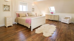 Een slaapkamer met een schuine plafond, een bed met een roze deken, een witte linnenkast, een stoel en een pluizig vloerkleed.