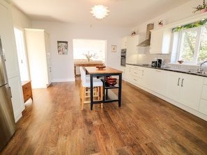 A modern kitchen with white cabinets, a wooden dining table, and a large window.