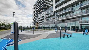 Un espacio exterior con equipo de ejercicio, una zona de juegos azul y un edificio moderno con balcones.