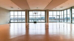 Amplio espacio interior con grandes ventanales, un aro de baloncesto y suelo de madera.