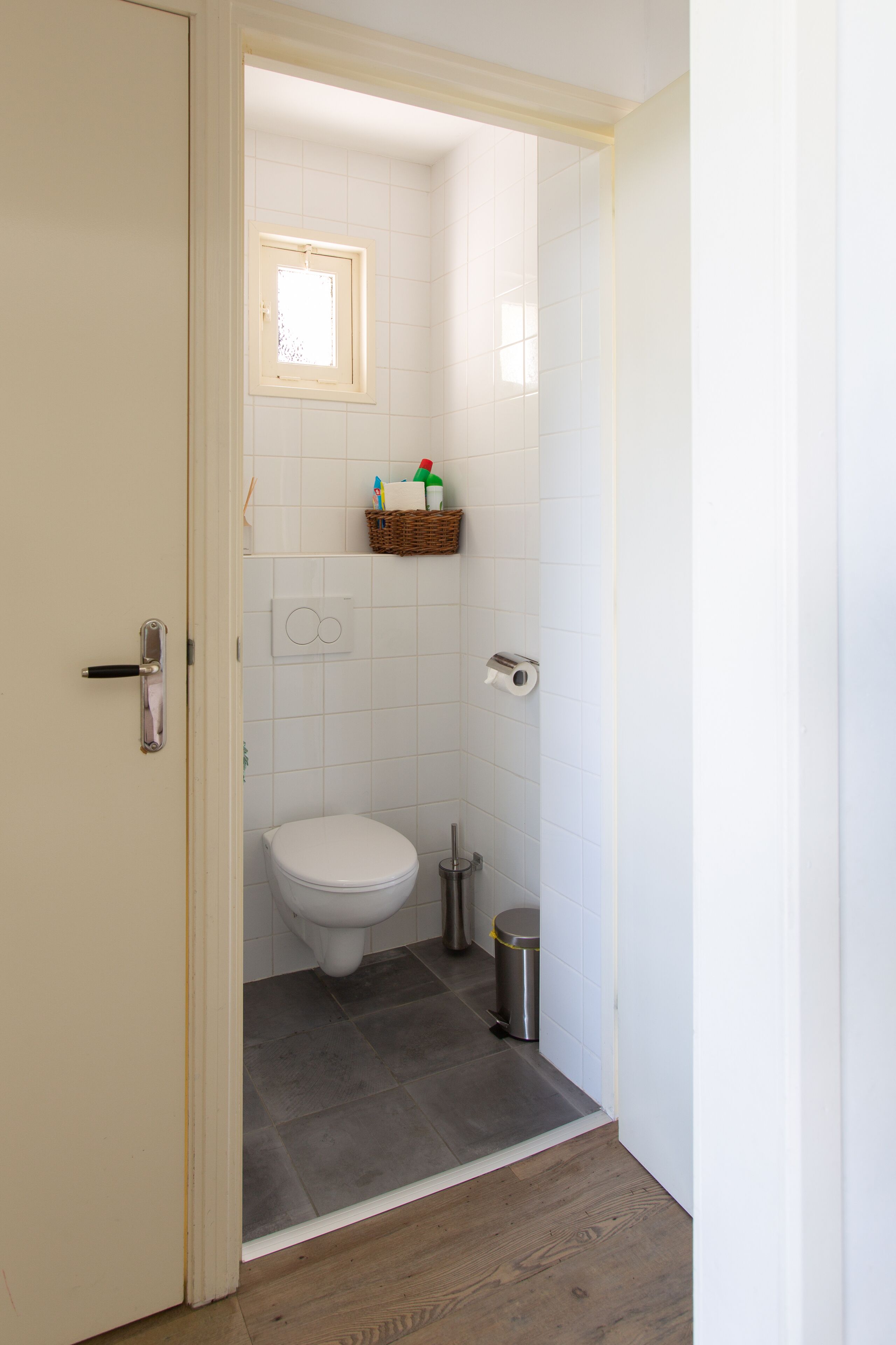 A small, clean bathroom with a toilet, a trash can, and a shelf with toiletries.