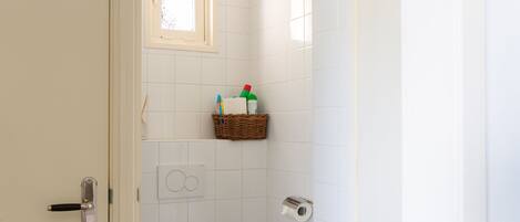 A small, clean bathroom with a toilet, a trash can, and a shelf with toiletries.