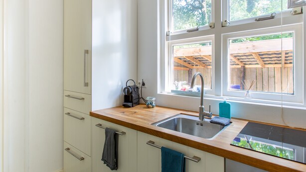 A modern kitchen with a wooden countertop, stainless steel sink, and white cabinets. There are multiple windows providing natural light and a view of the outdoors. - B&B Koepel Enschede (Enschede)