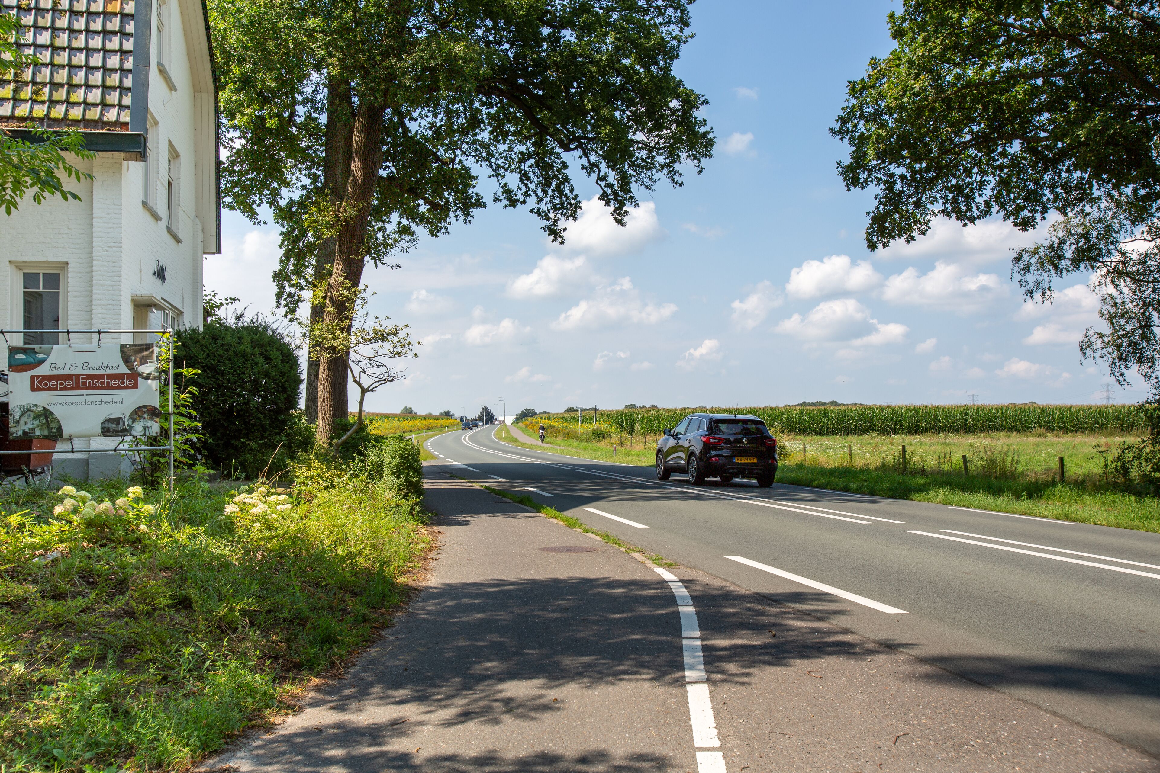 Une route avec une voiture, un bâtiment avec une enseigne et de la verdure.