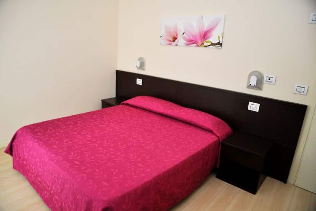 A neatly made bed with a red bedspread, a dark headboard, and a small bedside table with a lamp.