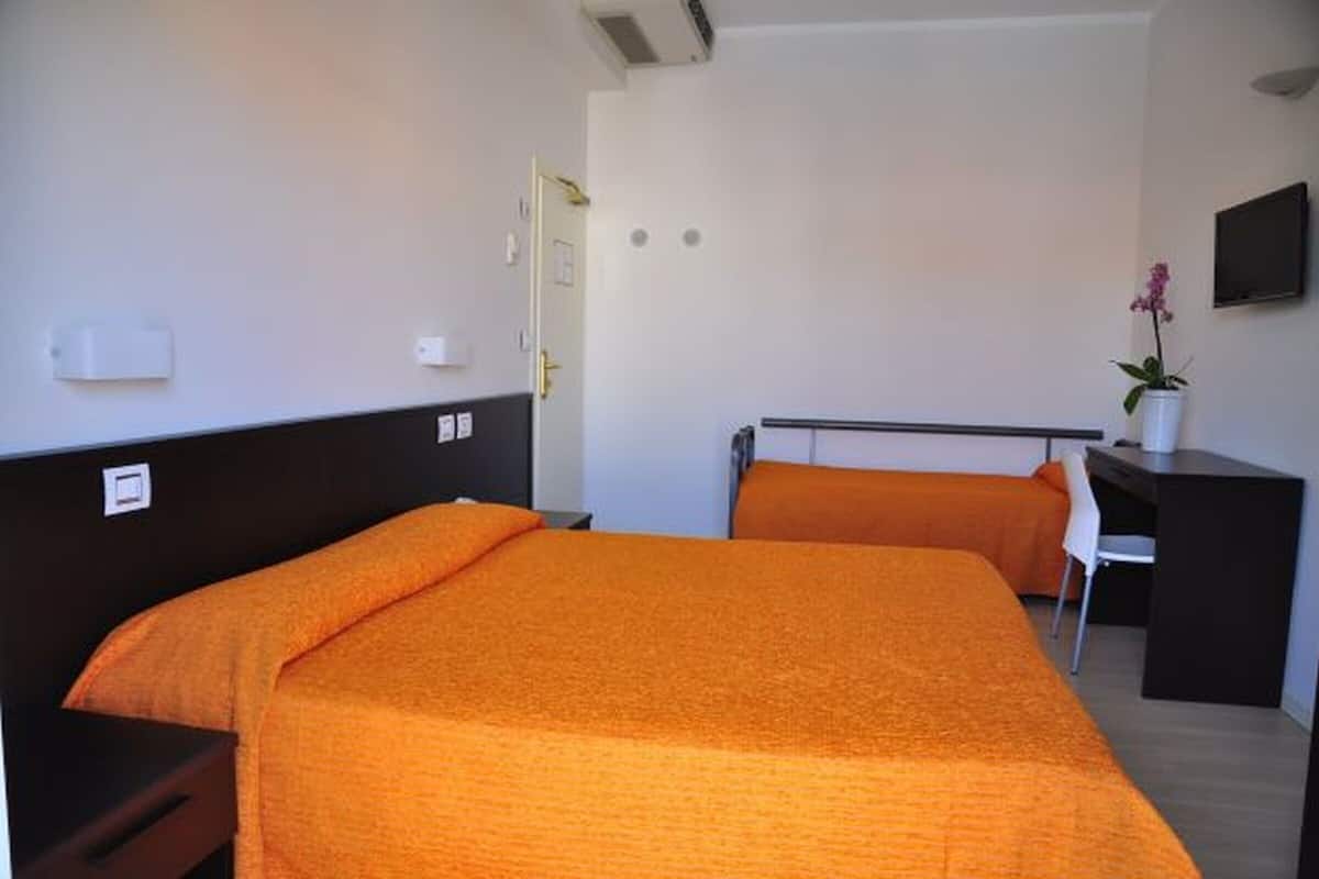 A hotel room with two beds, a desk, a chair, and a TV on the wall.