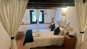 Un dormitorio con cama, cortinas, mesita de noche, lámpara y ventana.
