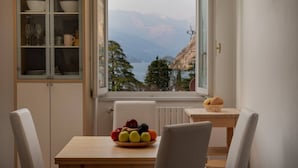Un coin repas avec une table dressée pour deux personnes, un panier de fruits sur la table et une vue sur les montagnes par la fenêtre.
