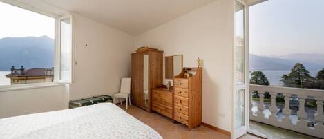Ein Schlafzimmer mit einem Bett, einer Holzkommode, einem Sessel und einem Balkon mit Bergblick.