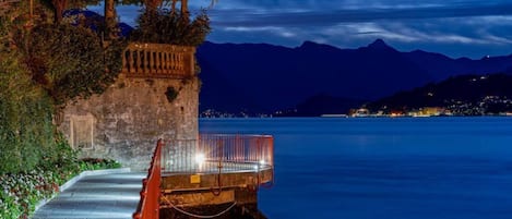 A stone pathway leading to a wooden gazebo by a calm body of water at night.