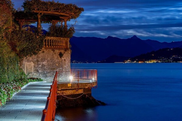 A stone pathway leading to a wooden gazebo by a calm body of water at night. - Casa Sole with lake view (Varenna)