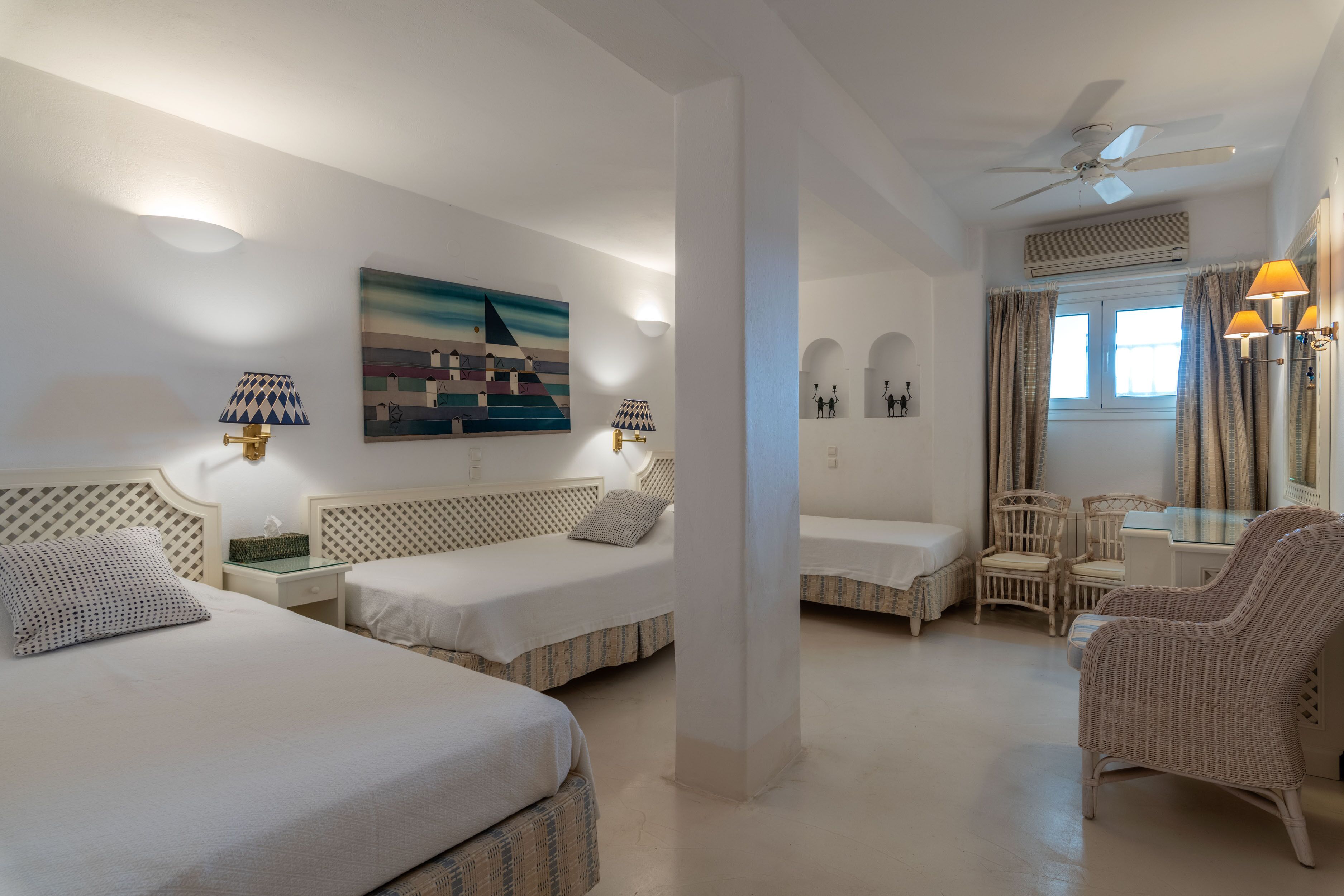 A hotel room with two beds, a dining area, and a large window with curtains.