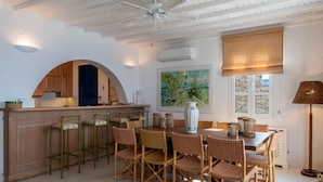 Un coin repas avec une table en bois et des chaises en osier, un bar avec des tabourets et un ventilateur de plafond.