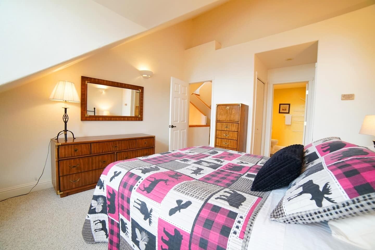 Une chambre à coucher comprenant un lit, une commode, un miroir et un escalier menant à une autre pièce.
