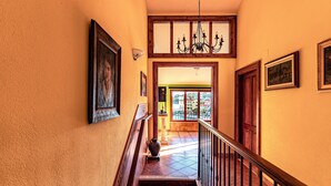 Una escalera con barandillas de madera y un candelabro, que conduce a una habitación luminosa con vistas al exterior.
