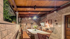 Un comedor con paredes de piedra, techo de madera, una mesa central y bancos.