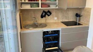 Uma cozinha compacta com máquina de lavar louça embutida, pia e prateleiras para louças e utensílios.