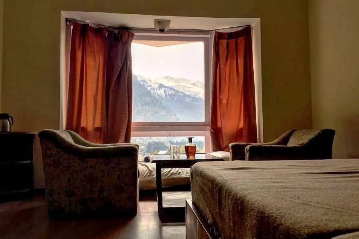 A room with a bed, two chairs, a small table, and a window with curtains.