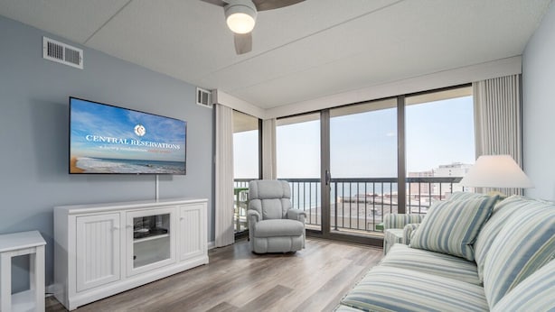 Een ruime woonkamer met een grote tv waarop 'Central Reservations' staat, een balkon met uitzicht en een plafondventilator.