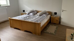 A bedroom with a wooden bed, two bedside tables, a radiator, a window, and a door. - Vacation apartment in the countryside (Lebach Landsweiler)