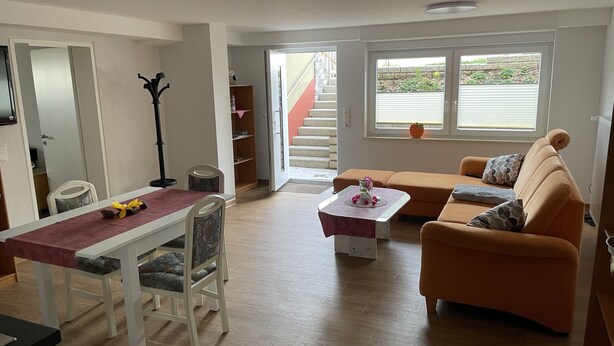 A living room with a dining table, a sofa, and a staircase leading to an outdoor area. - Vacation apartment in the countryside (Lebach Landsweiler)