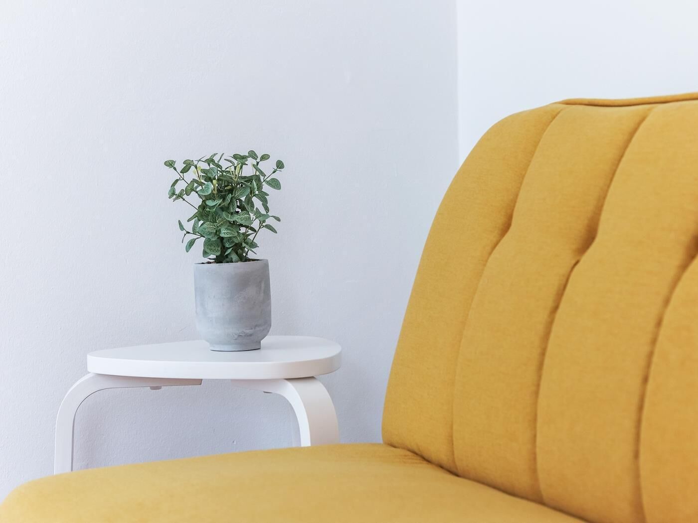 Una silla color mostaza con una mesita auxiliar blanca a su lado.