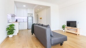 En modern lägenhet med en grå soffa, en tv, ett kök och en matplats.