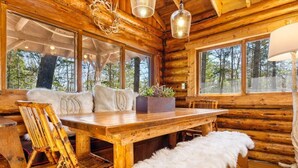 A log cabin interior with a wooden dining table, chairs, and a fur throw. - Chic, updated log cabin nestled in the pine trees of Sprucewold! (Boothbay Harbor)