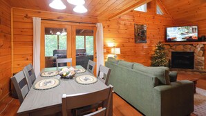 L’intérieur d’un chalet en bois comprend une table à manger, des chaises, un canapé vert, une cheminée et un téléviseur.