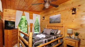 Une chambre à coucher dans un chalet en bois, avec un lit, une table de chevet, un téléviseur et un tableau accroché au mur.