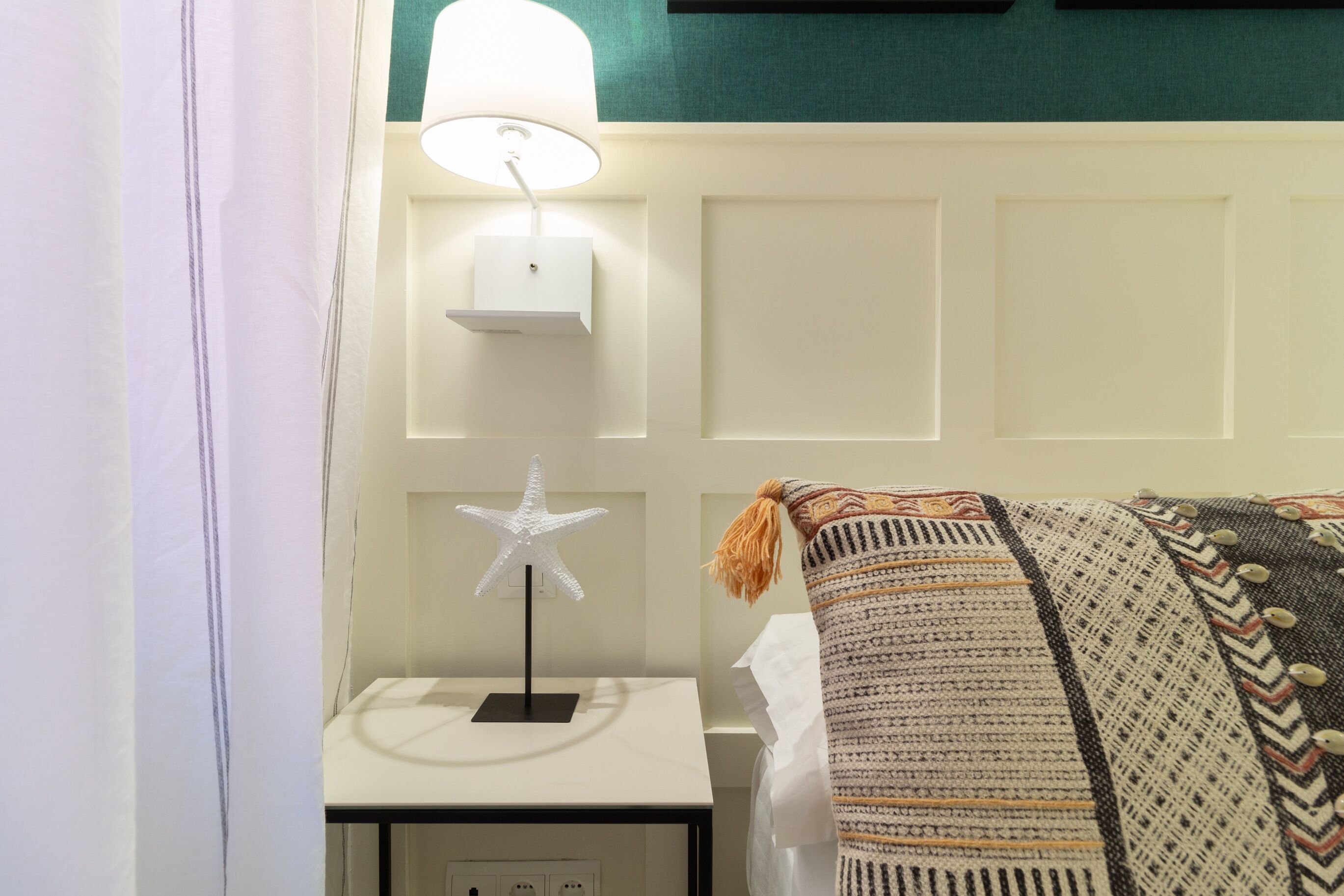 Una cama bien hecha con un edredón estampado, una lámpara de noche con forma de estrella en una mesita de noche y una lámpara de pared.
