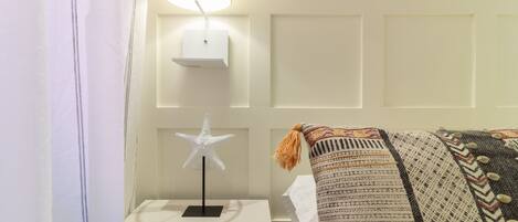 Una cama bien hecha con un edredón estampado, una lámpara de noche con forma de estrella en una mesita de noche y una lámpara de pared.