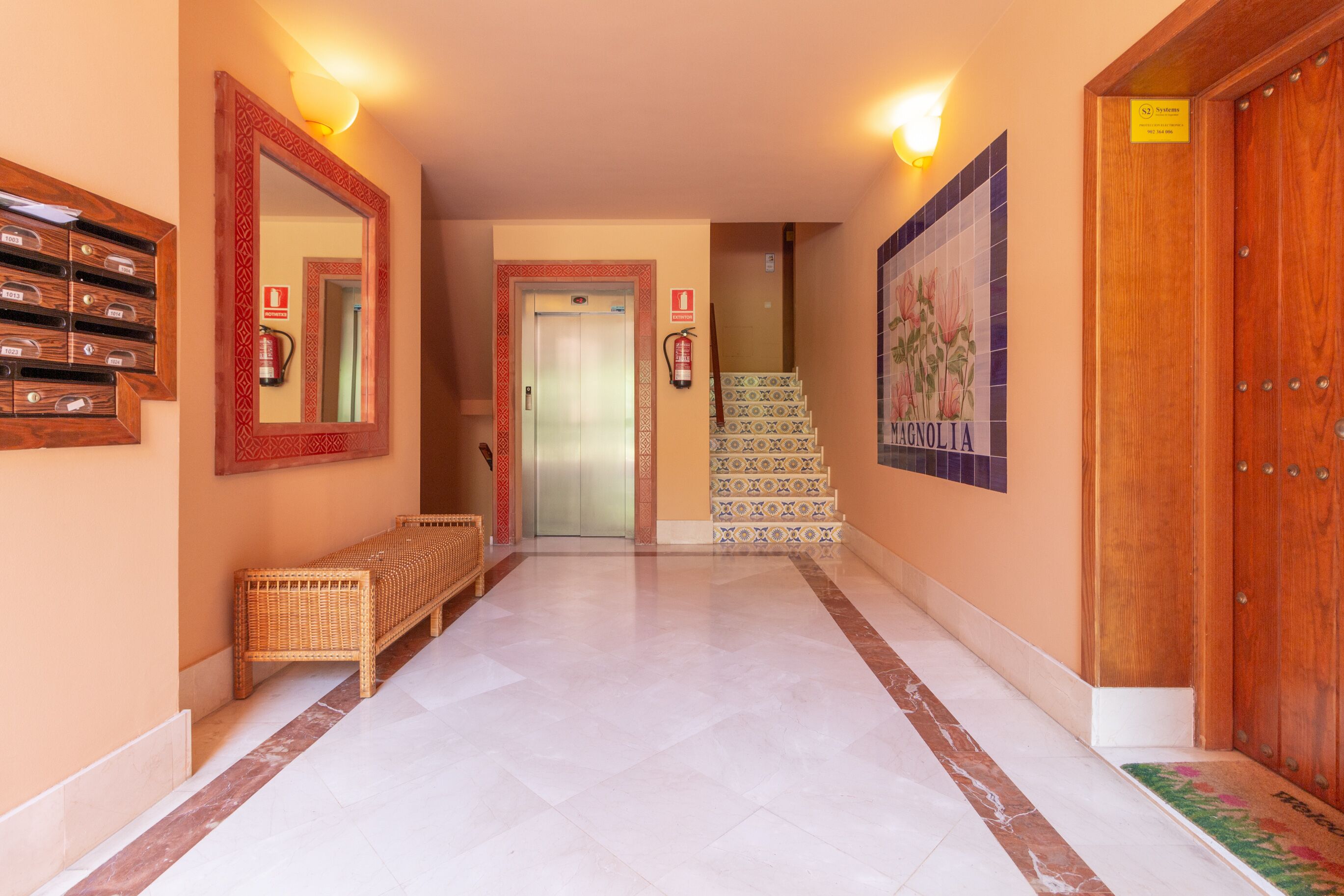 A hallway with a wooden bench, a mirror, a fire extinguisher, a staircase, and a door with a sign.