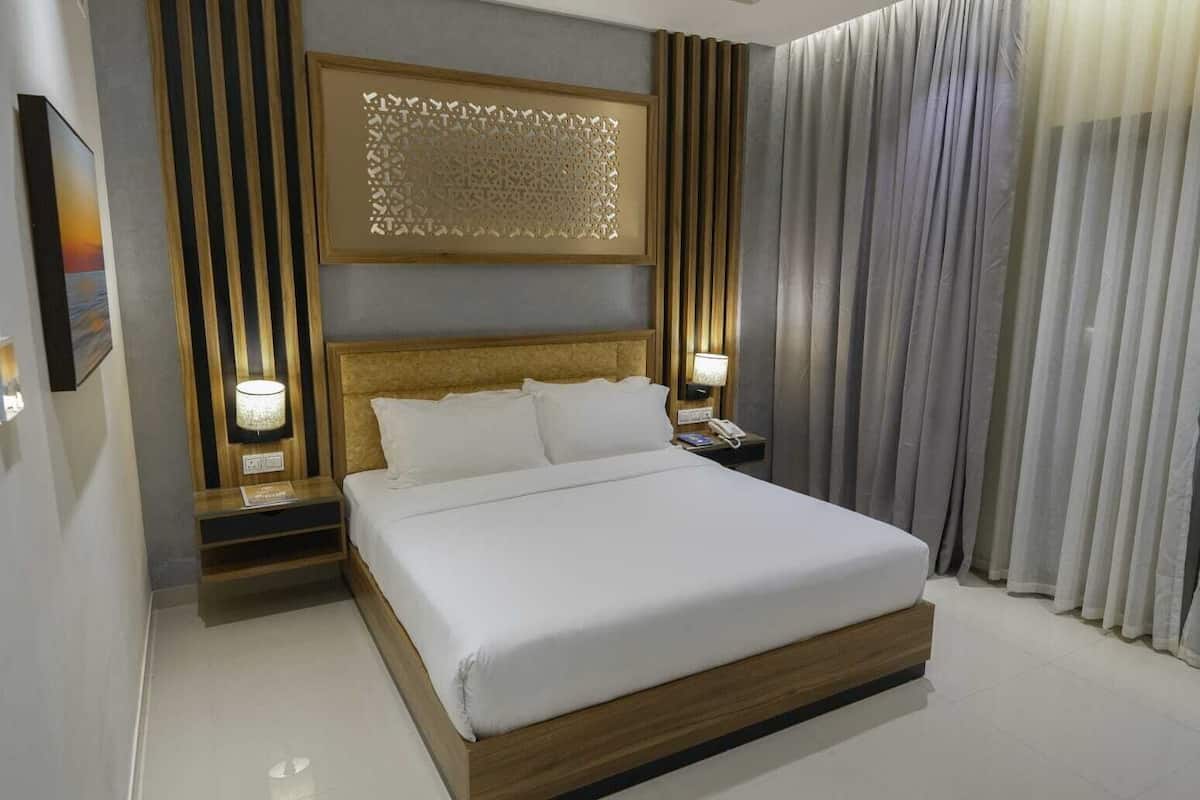 Habitación de hotel moderna con una cama grande, cabecera de madera y un panel decorativo en la pared. Hay dos mesitas de noche con lámparas y un teléfono.