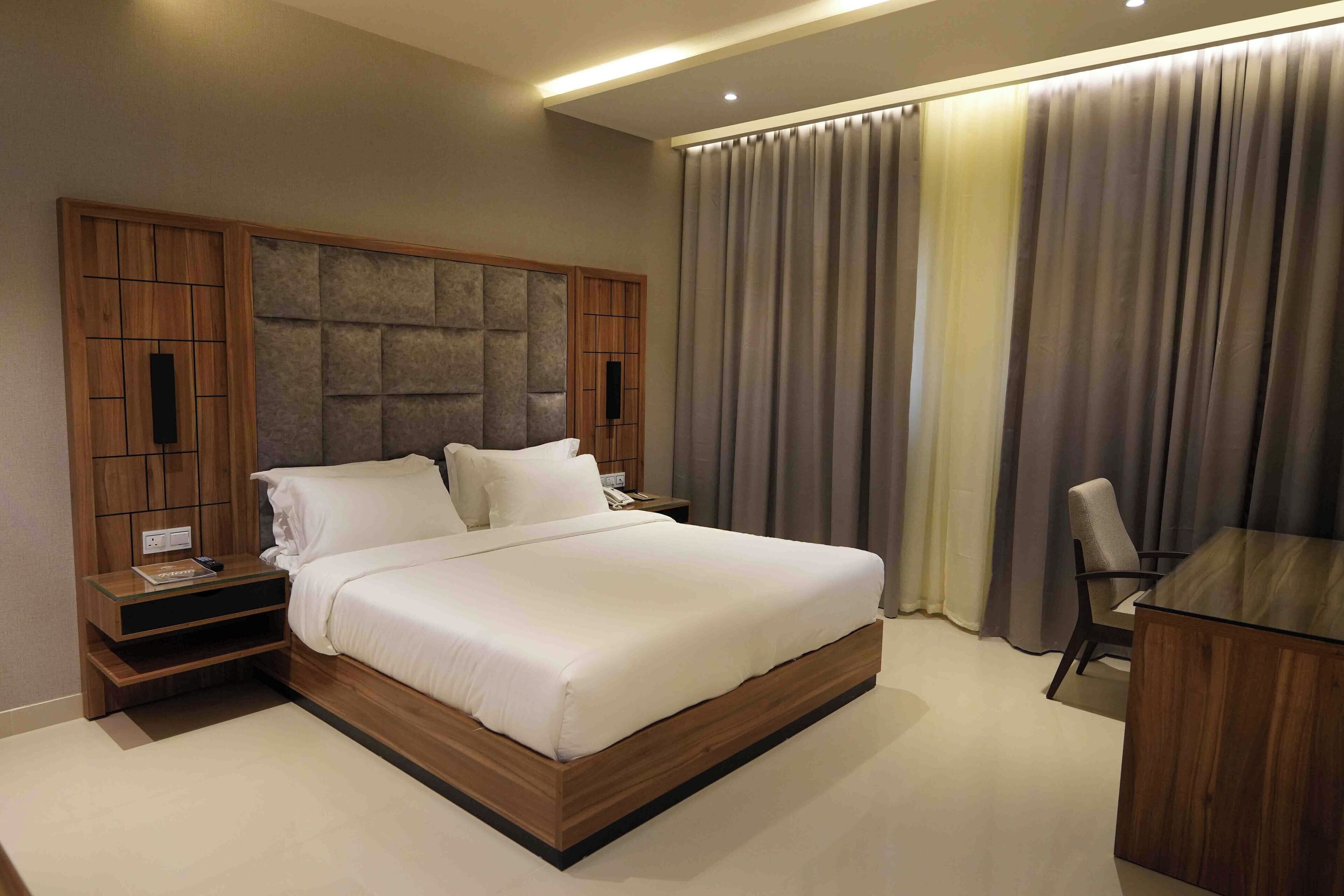 Une chambre d’h ôtel moderne avec un grand lit, une tête de lit en bois, une table de chevet, un bureau et une chaise.