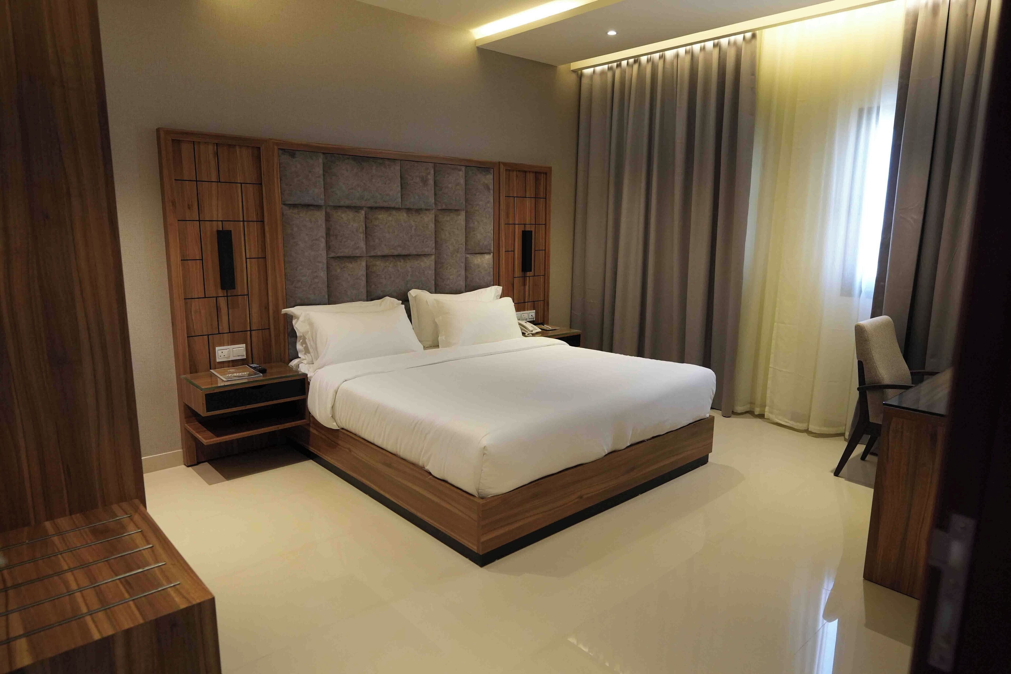 A modern hotel room with a large bed, wooden headboard, bedside tables, and a desk.
