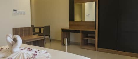 A hotel room with a large bed, a wooden desk, a chair, a small trash bin, and a wardrobe.