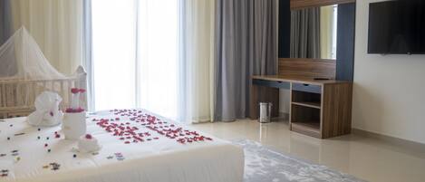 A hotel room with a bed, a TV, a desk, and a large window with curtains.