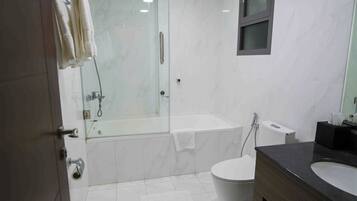 Un baño moderno con ducha de vidrio, bañera, inodoro y tocador con lavamanos.