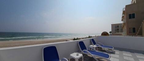 Eine Dachterrasse mit blauen Liegestühlen und Blick auf den Strand.