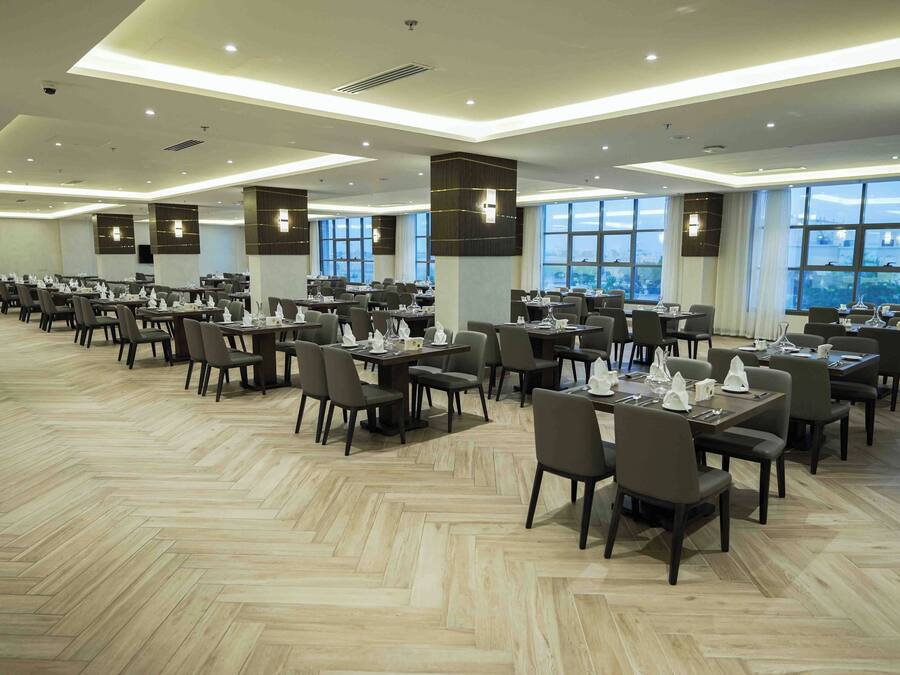 A spacious dining area with multiple tables and chairs, large windows, and a modern ceiling design.