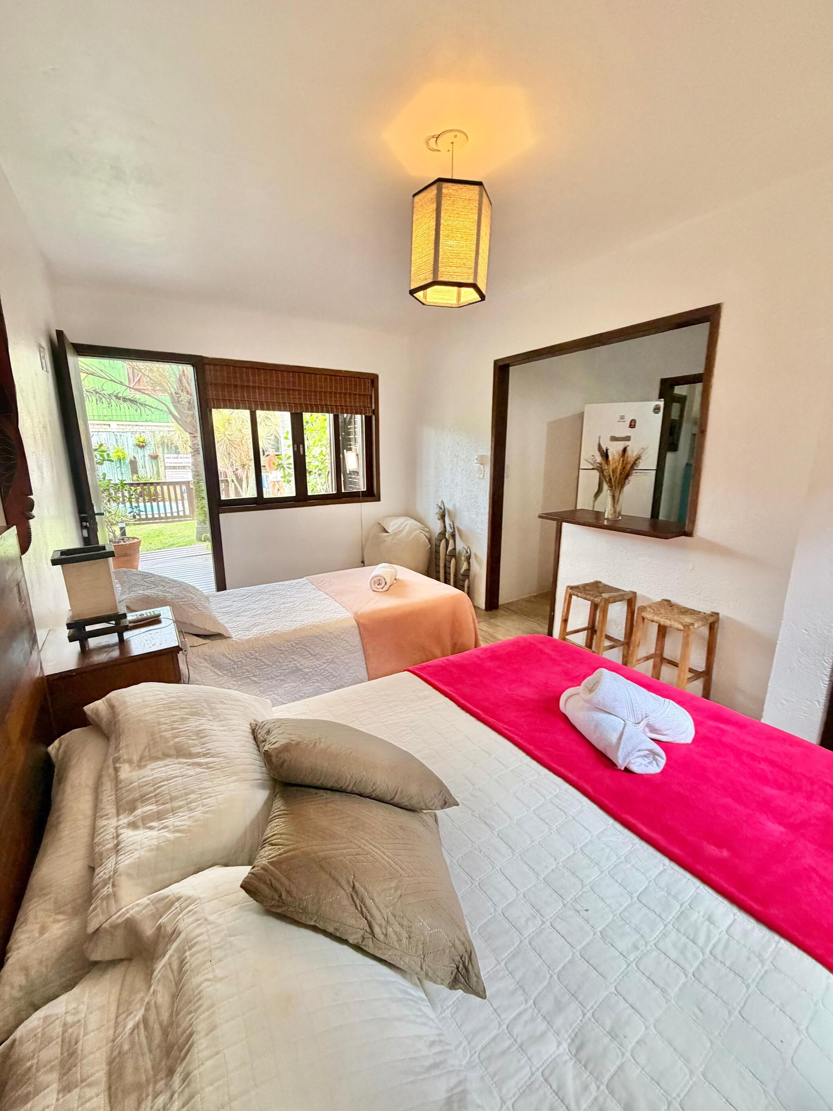 Habitación de hotel con dos camas, un ventanal grande, un espejo y una lámpara en el techo.
