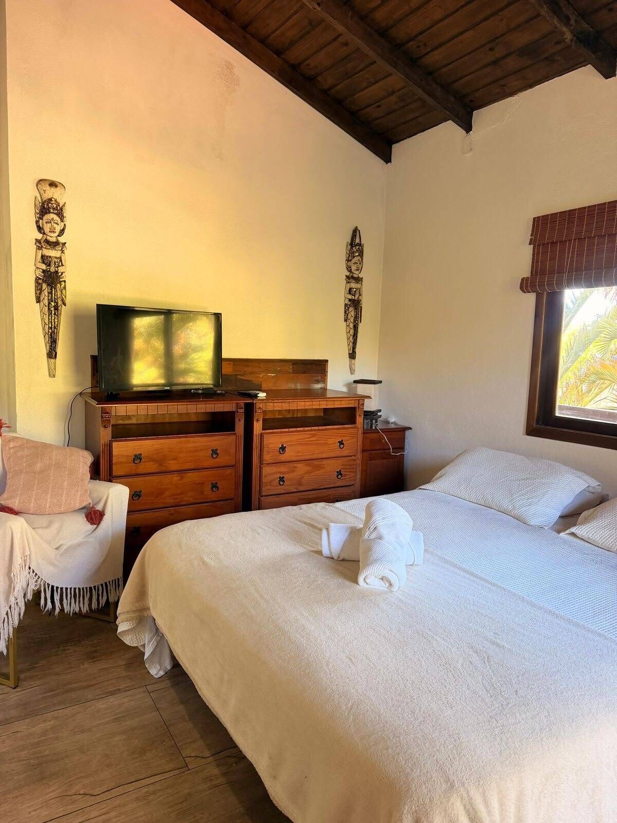 A bedroom with a bed, wooden dresser, television, and decorative wall art.