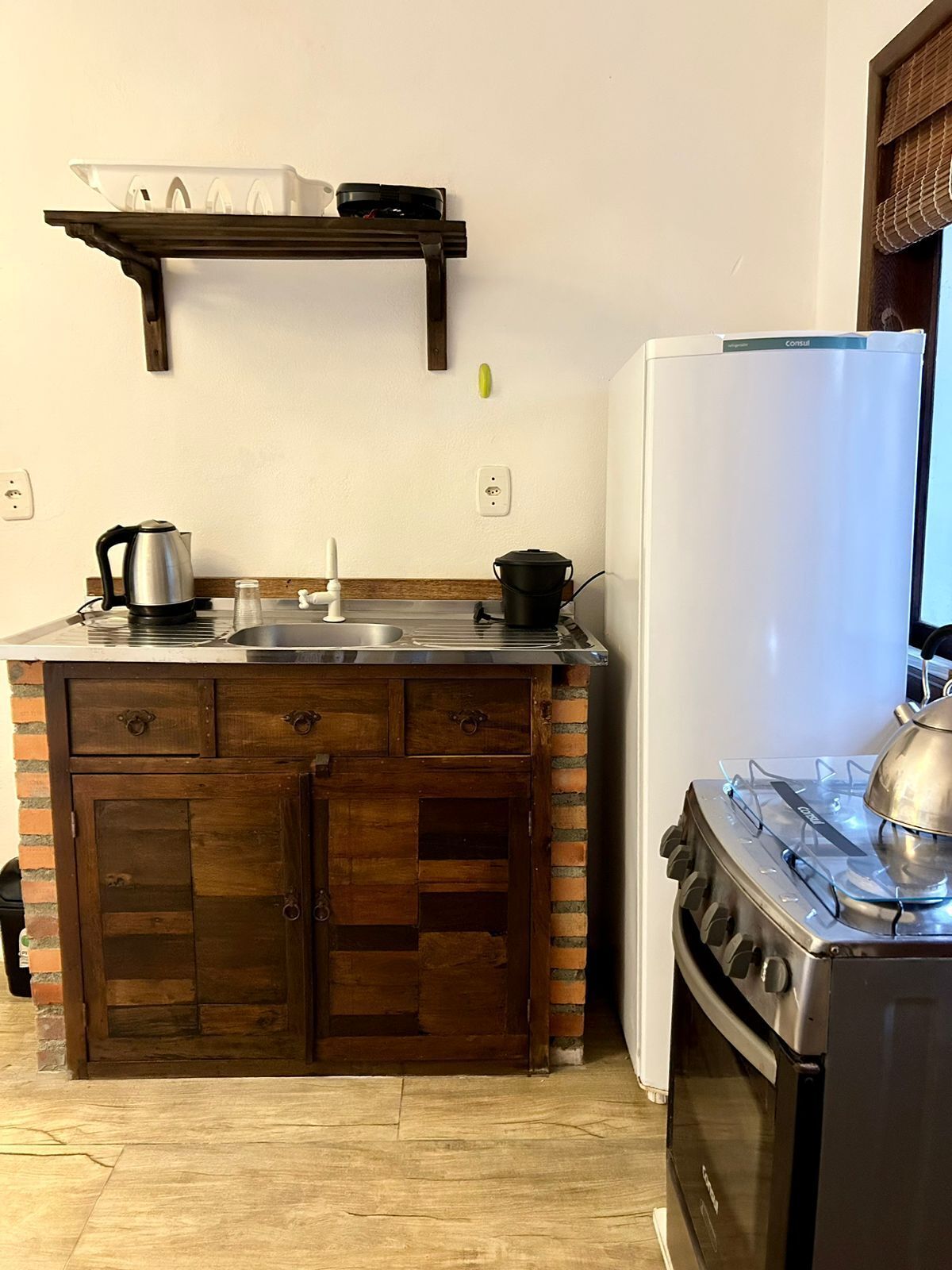 A compact kitchen with a wooden cabinet, a sink, a stove, and a refrigerator.