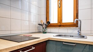 Una cucina con piastrelle bianche, una finestra in legno, un lavello in acciaio inossidabile e un piano di lavoro in legno.